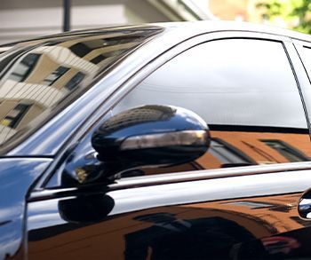 Close-up of a black car door and side mirror reflecting nearby buildings.