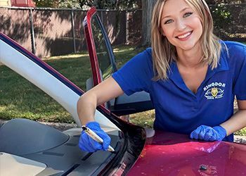 Woman in blue shirt and gloves cleaning a car windshield outdoors.