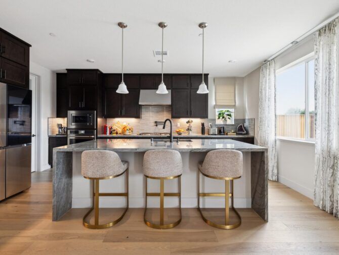 Modern kitchen with dark cabinetry, gray island, and three gold-legged bar stools.