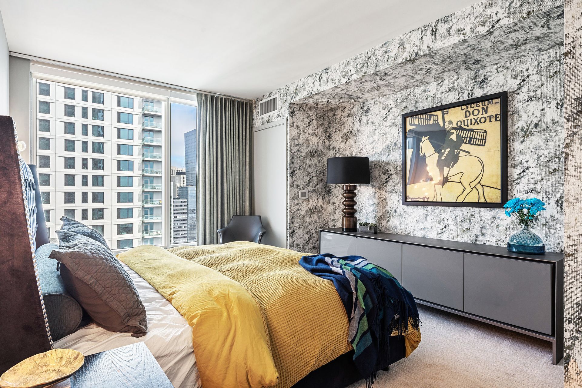 Bedroom with marble wallpaper, yellow and blue bedding, and a cityscape view.