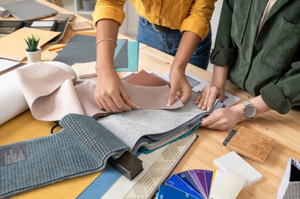 Two people examining fabric swatches on a wooden table; interior design.
