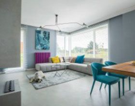 A modern living room with a sectional sofa, teal chairs, and a dog on a rug.
