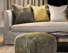 Couch with gray, gold and textured pillows, with a matching ottoman in front.