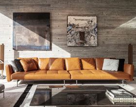 Modern living room with orange leather sofa, art on concrete wall, and glass coffee table.