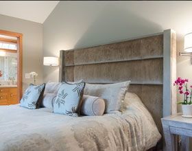 Bedroom with large upholstered headboard, neutral tones, decorative pillows, bedside table with lamp and orchid.