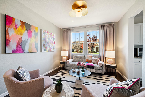 Living room with abstract art, blush armchairs, and a gray sofa, featuring a window view and a patterned rug.