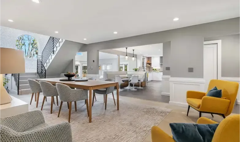 Open-concept dining/living area with table, chairs, yellow armchairs, stairs, and a view into the kitchen.