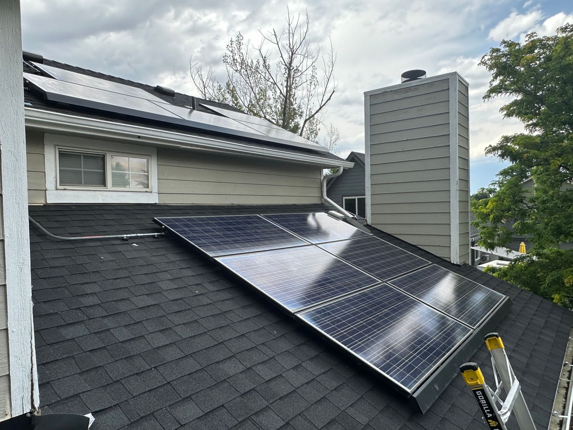 House with solar panels on roof, sunny day, blue sky, green lawn, and evergreen trees.