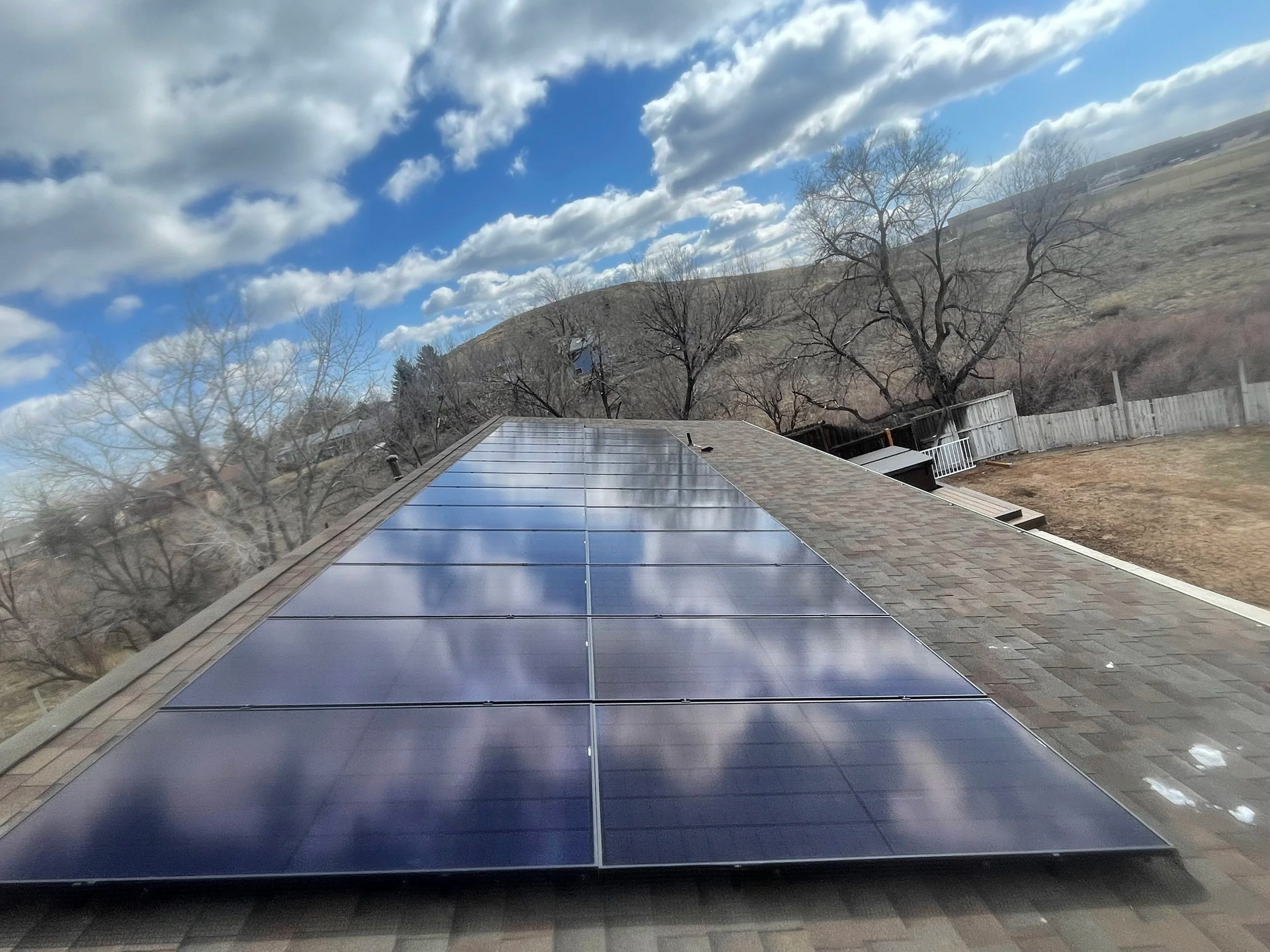 Wooden house with solar panels on the roof, surrounded by trees and greenery.