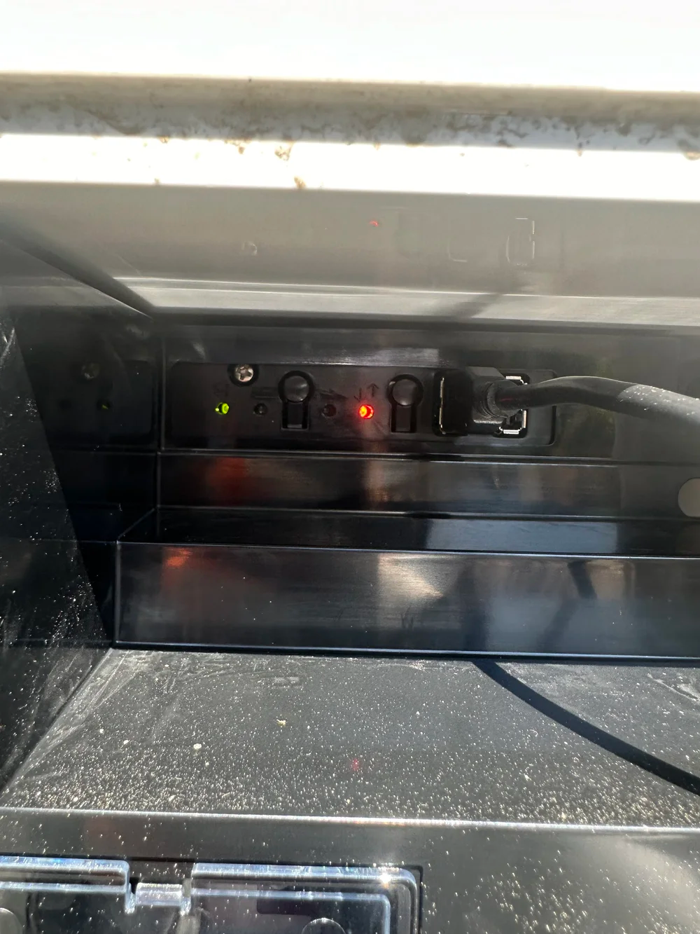 Black electrical panel with green and red lights; power cord plugged in.