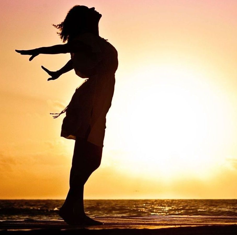 A silhouette of a woman standing on a beach with her arms outstretched
