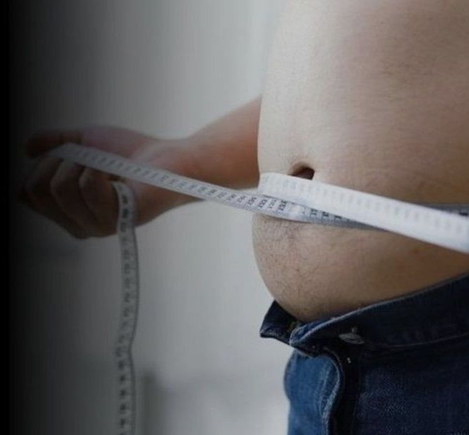 Person measuring their belly with a white measuring tape; jeans visible.