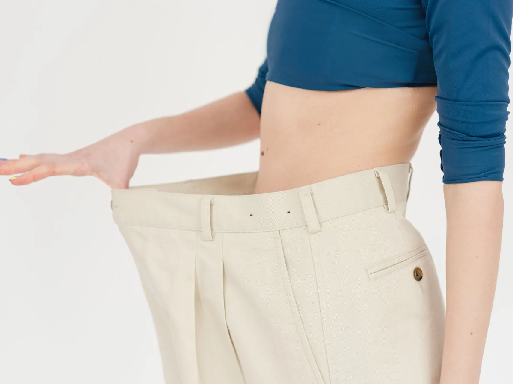 a woman in a blue crop top is measuring her pants