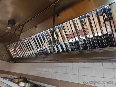 A kitchen with a stainless steel exhaust fan hanging from the ceiling.
