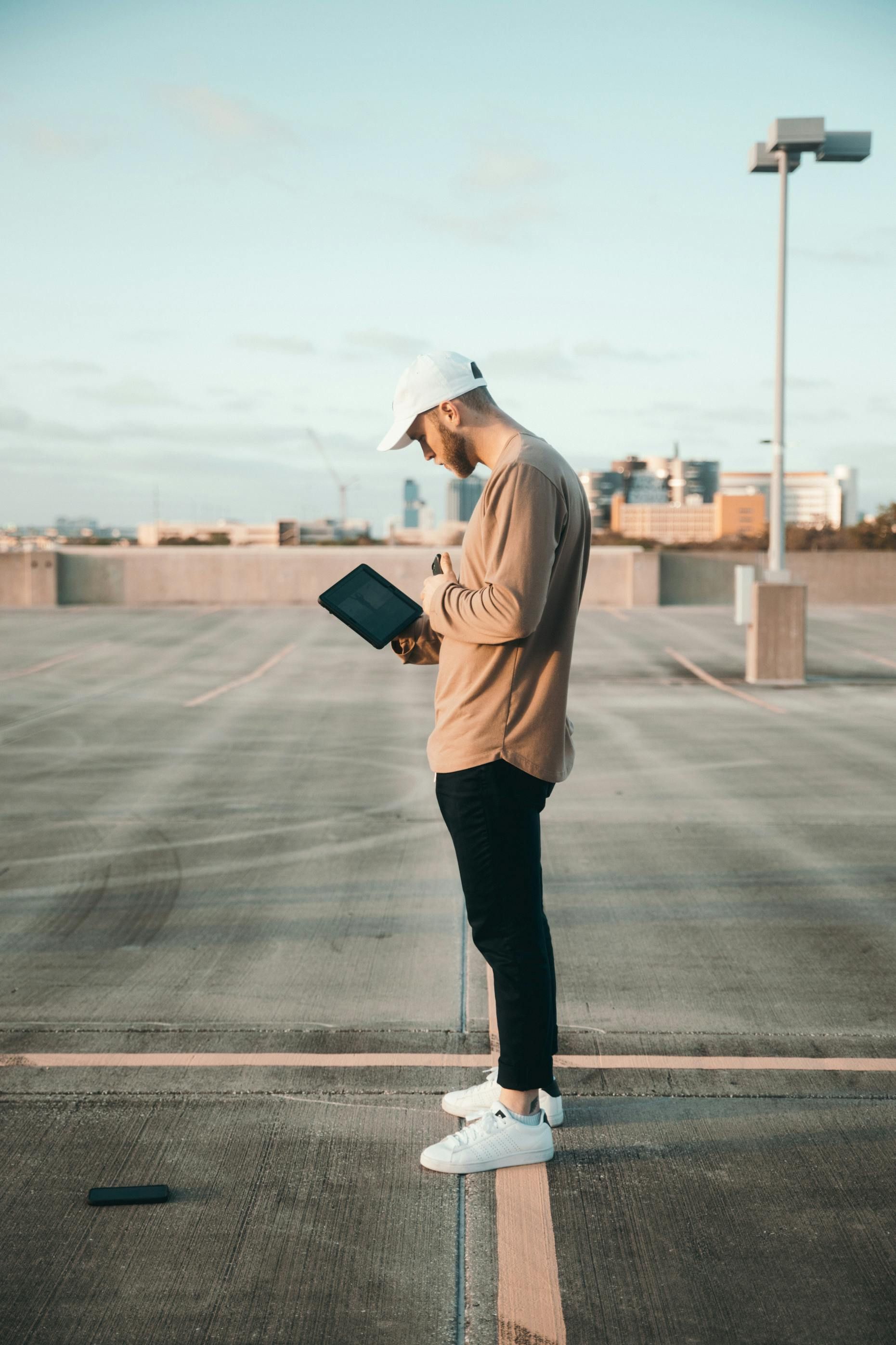 Un homme portant une casquette et des vêtements décontractés regarde une tablette sur le toit d'un parking.