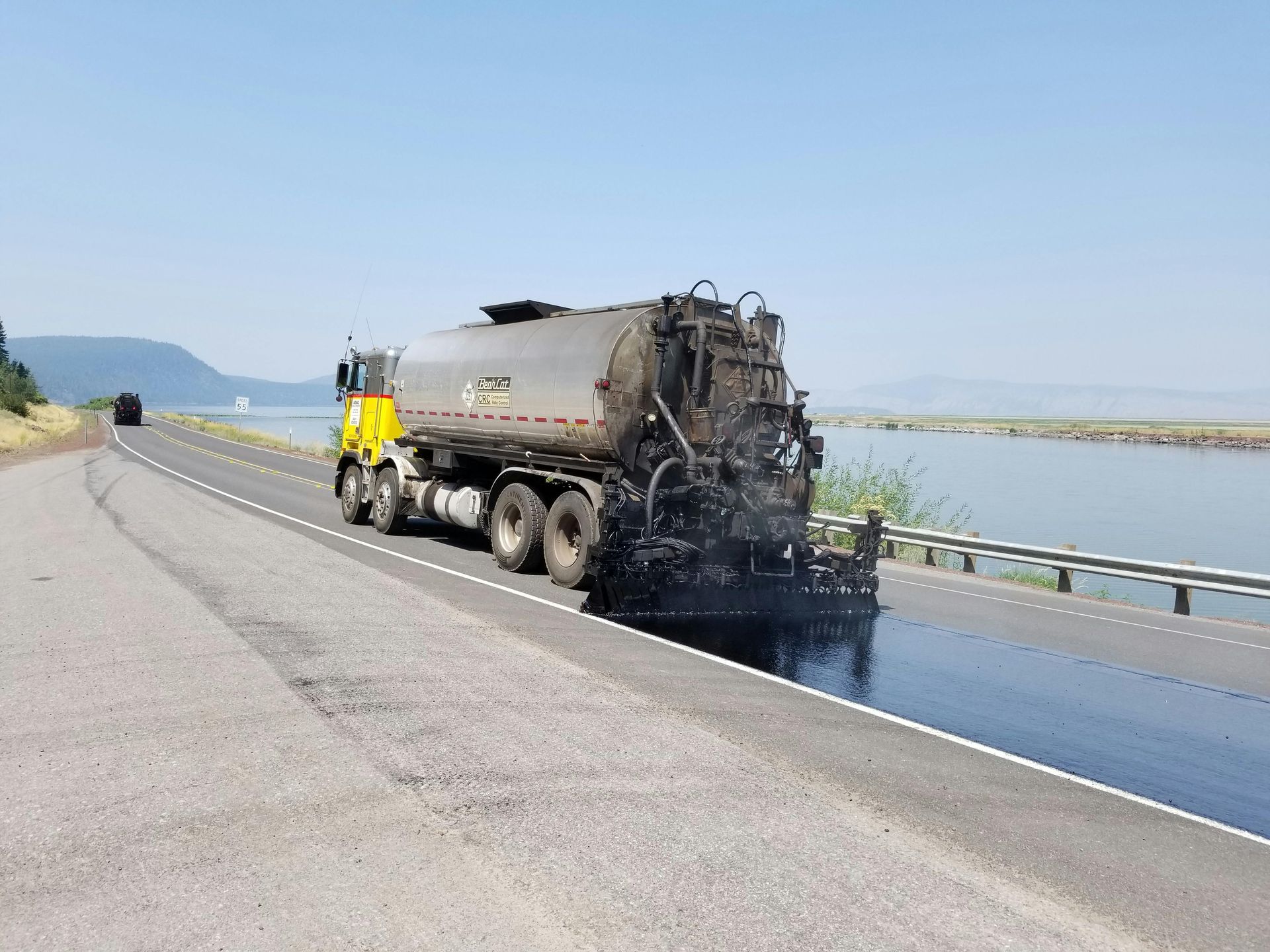 Un camion d'asphalte pave une route près d'un plan d'eau par une journée ensoleillée.