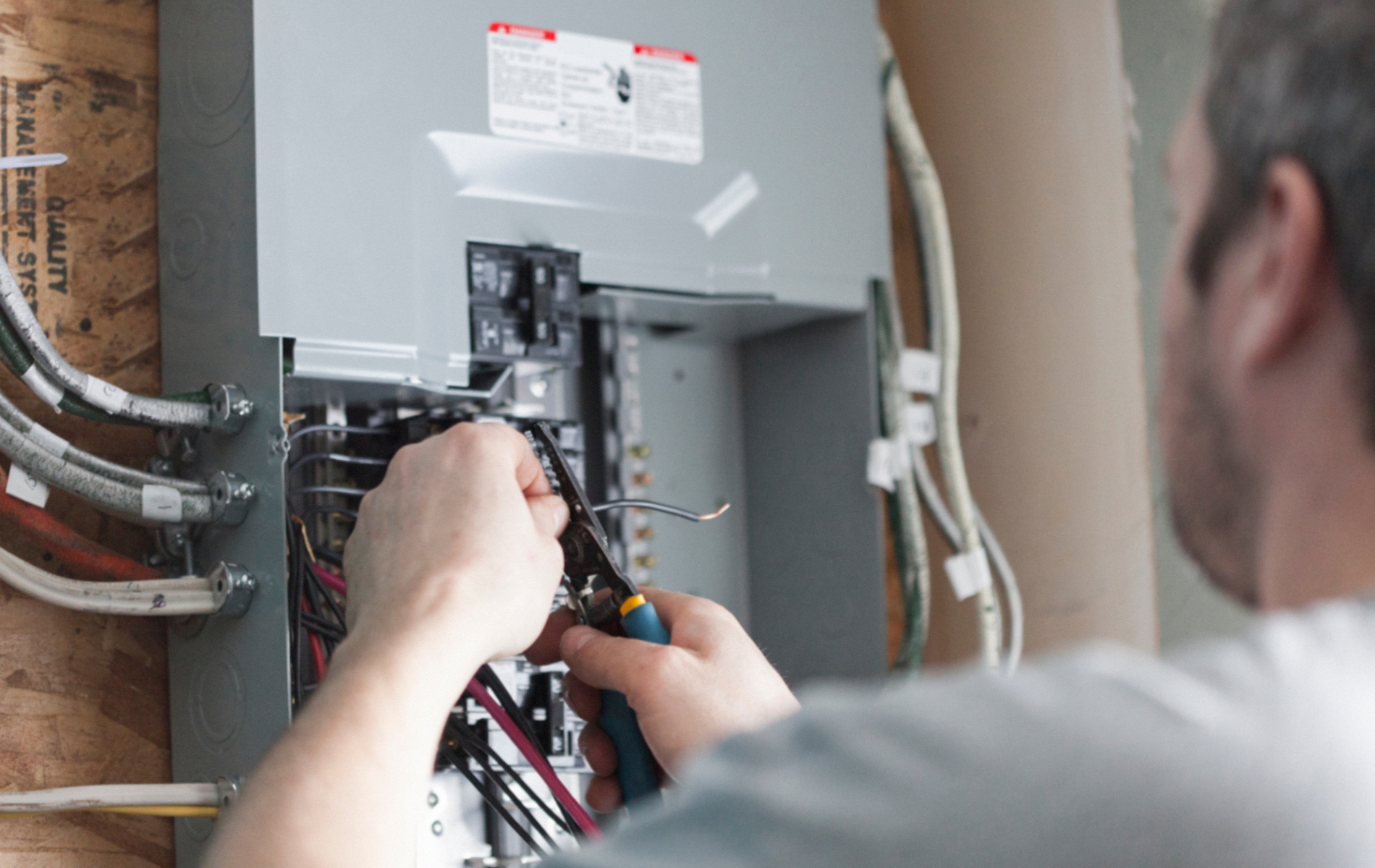 A person installing electrical wiring in a gray breaker box on a wood wall.