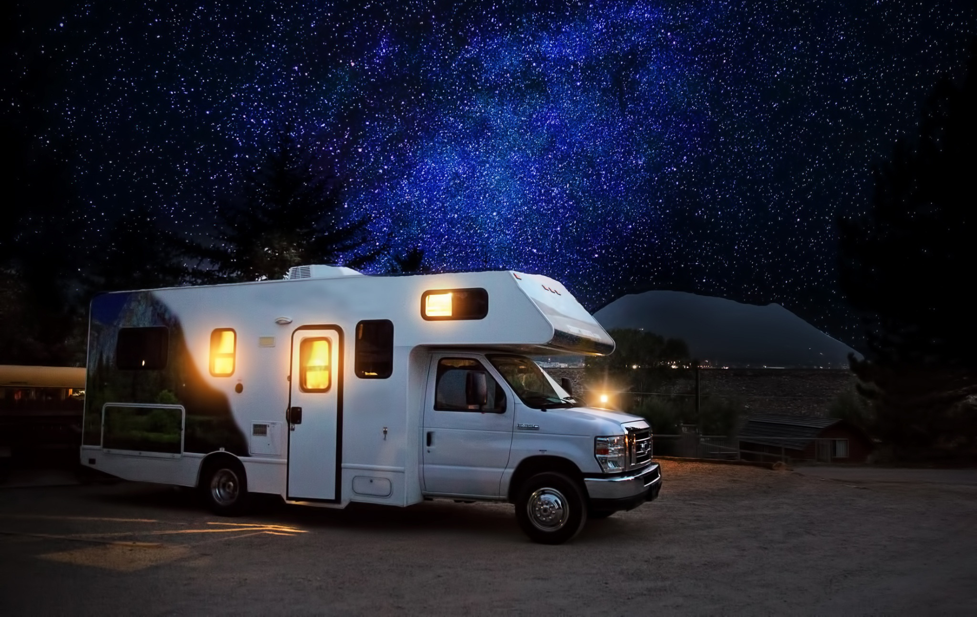 White RV parked under a starry night sky with lit windows, suggesting a camping scene.