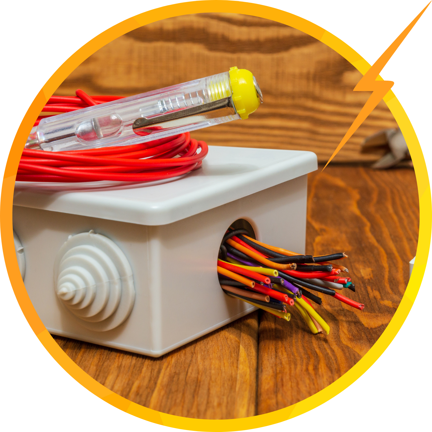 Electrical box with exposed wires, red wire spool, and voltage tester on wood surface.
