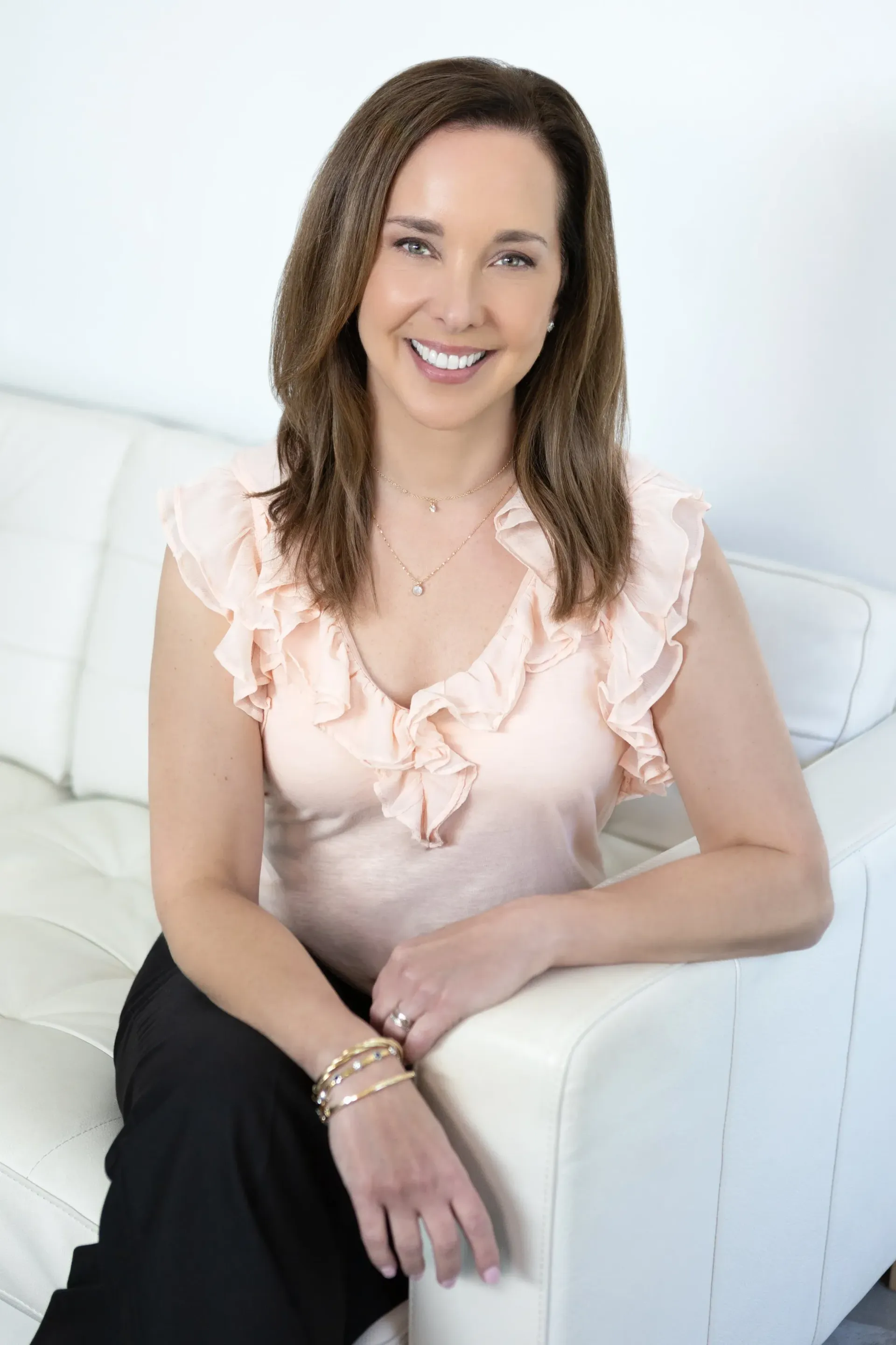 Woman in pink top smiles, sitting on white couch.