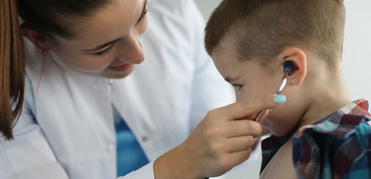 Doctor examining a child’s ear with an otoscope in a clinic