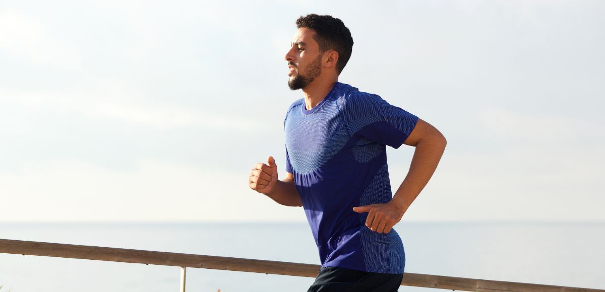 Man running along a waterfront in a blue shirt and dark shorts under a clear sky