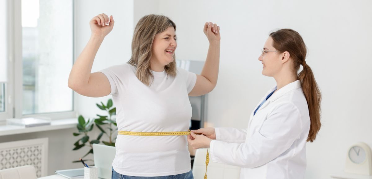 Doctor measuring a smiling patient’s waist in a bright clinic