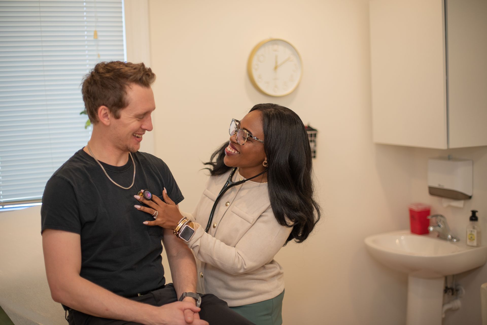 Doctor listening to patient's chest with a stethoscope in an examination room. They are both smiling.