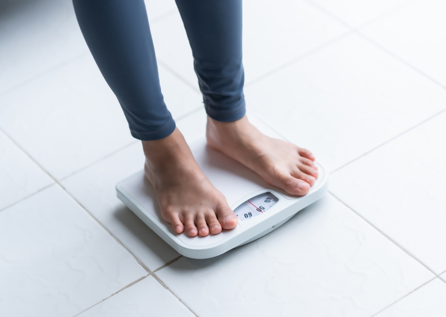 Bare feet standing on a white scale, wearing dark blue leggings, in a room with white tile.