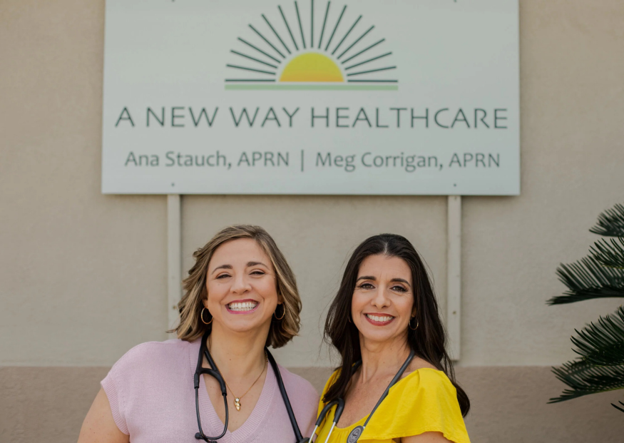 Two women smiling in front of a clinic sign: