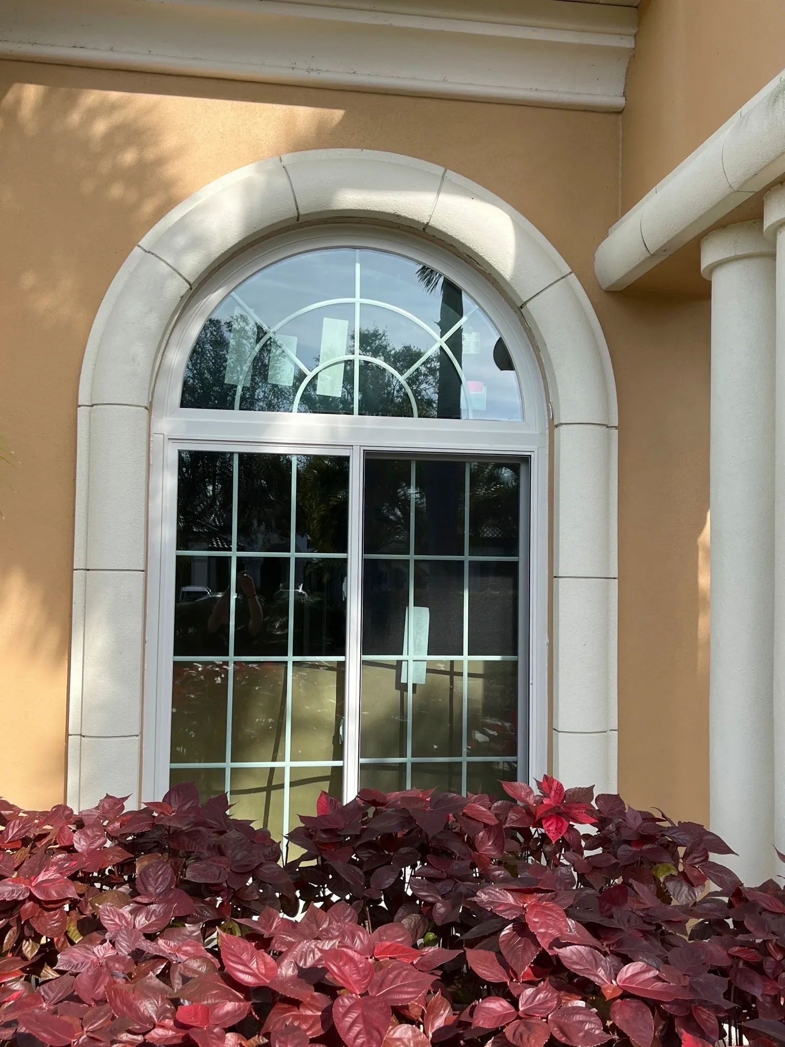 A house with a large arched window and a bush in front of it