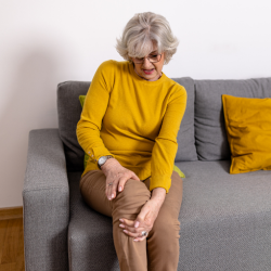 a woman in a yellow sweater is sitting on a couch holding her knee with Chronic Pain