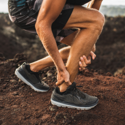 a man is kneeling down and holding his ankle in pain with Tendonitis 