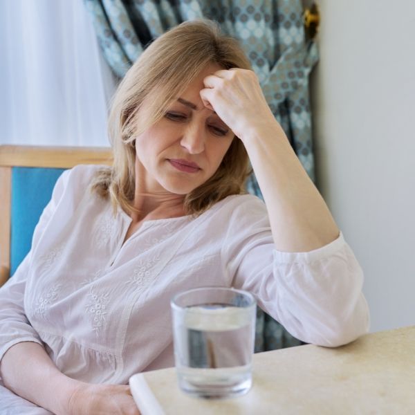 A woman is sitting at a table with a glass of water dealing with a migraine or headache