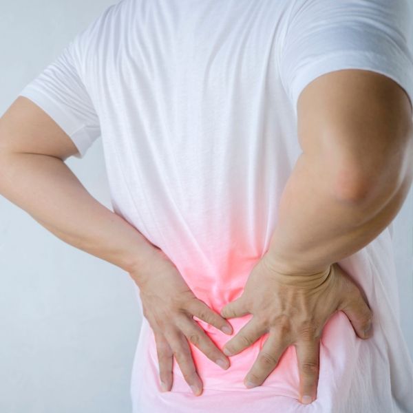 A man in a white shirt is holding his lower back in pain.