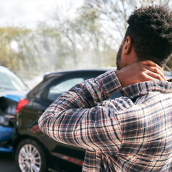 a man in a plaid shirt is holding his neck in pain in front of a car accident with whiplash