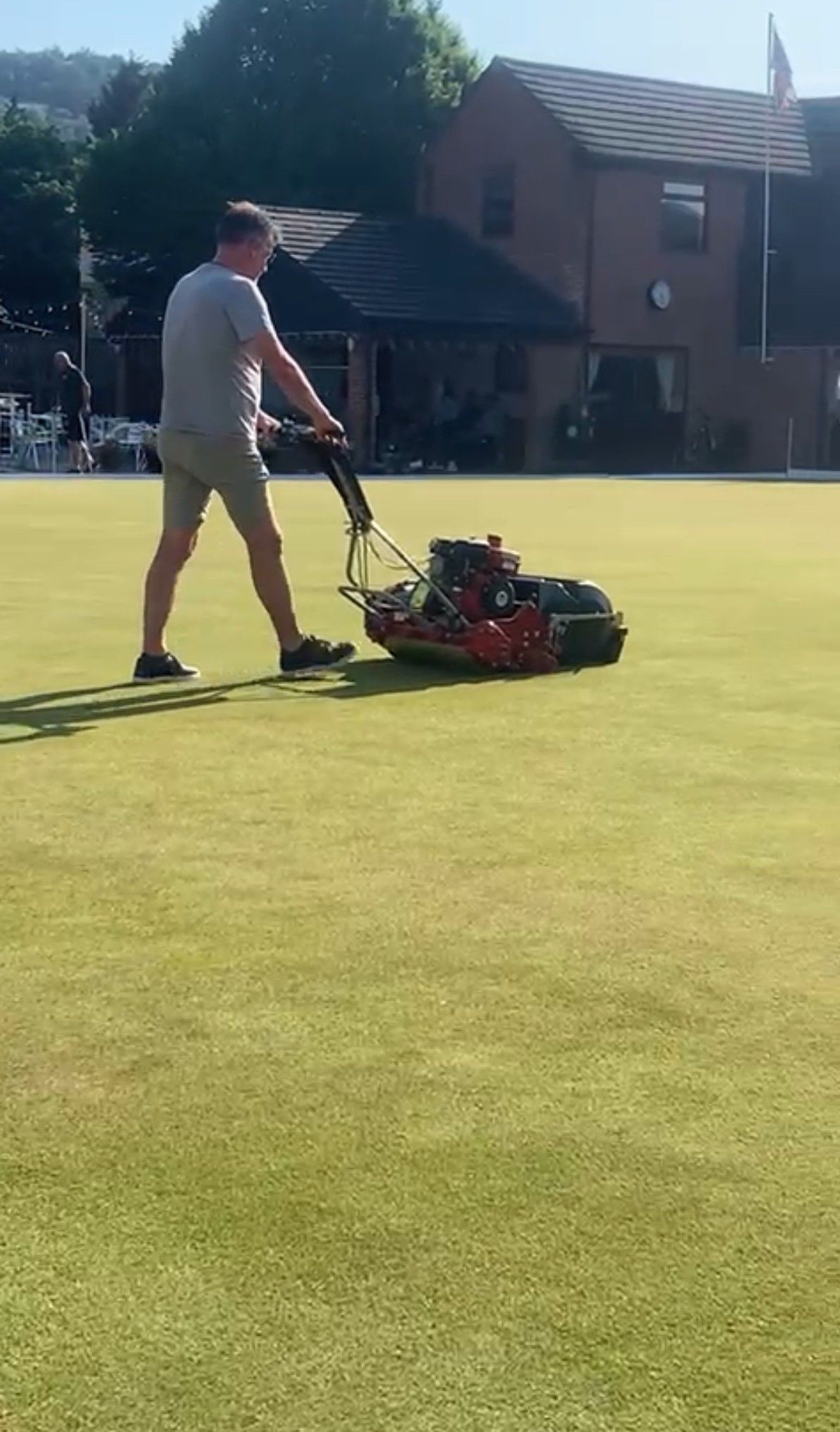 Man mowing a green lawn with a red lawnmower in front of a building.
