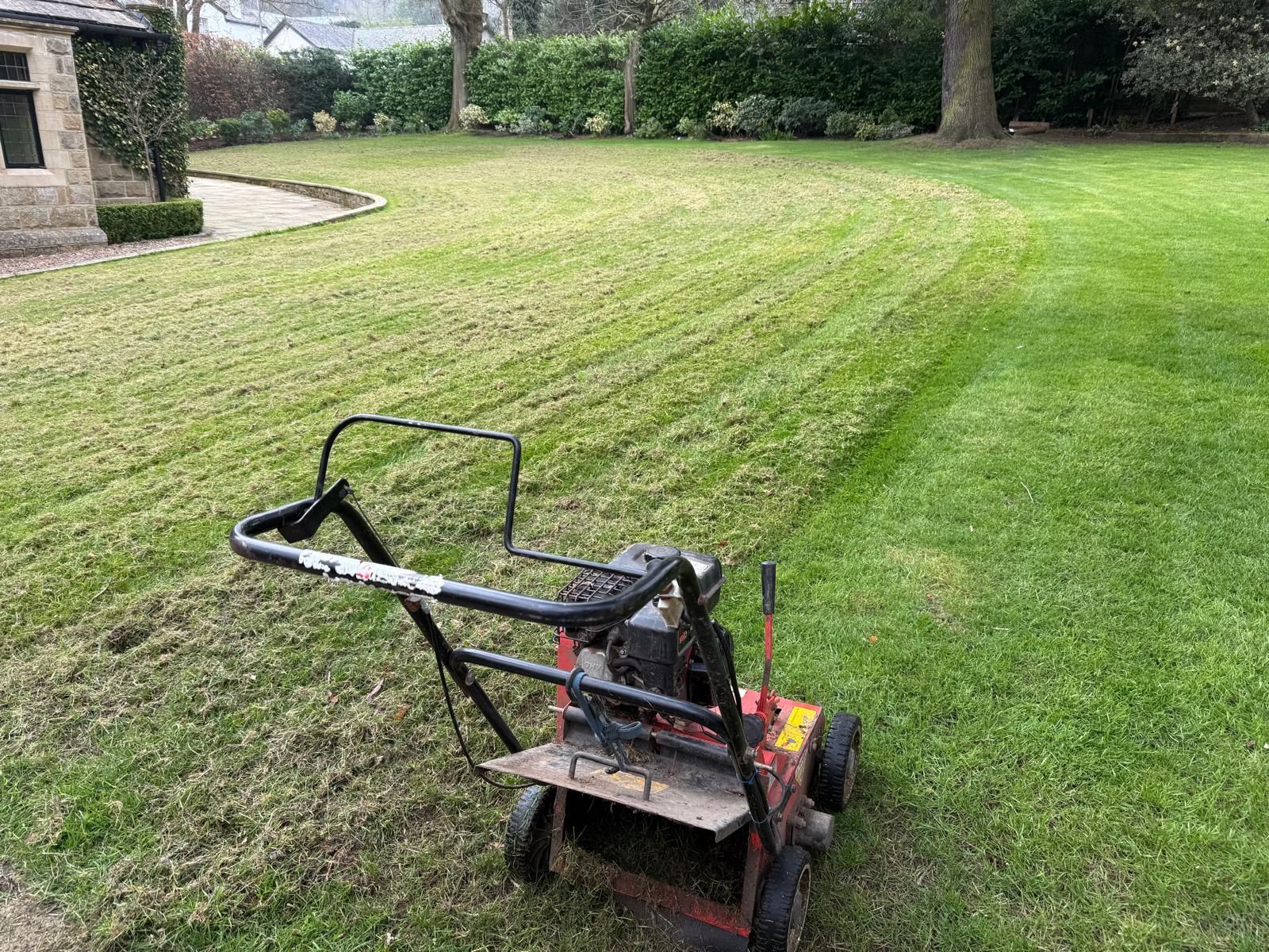 Lawn being aerated with a machine. Green grass with visible lines, stone building in background.