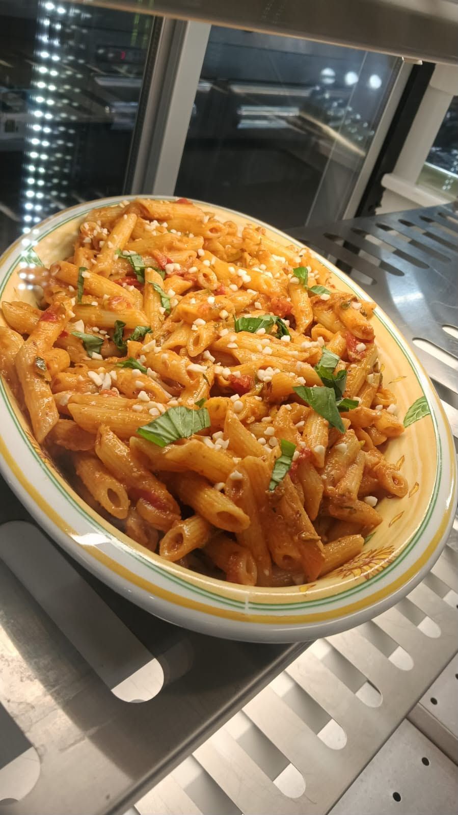Una ciotola di penne al sugo di pomodoro con erbe aromatiche e formaggio grattugiato, servita su un vassoio vicino a una finestra.