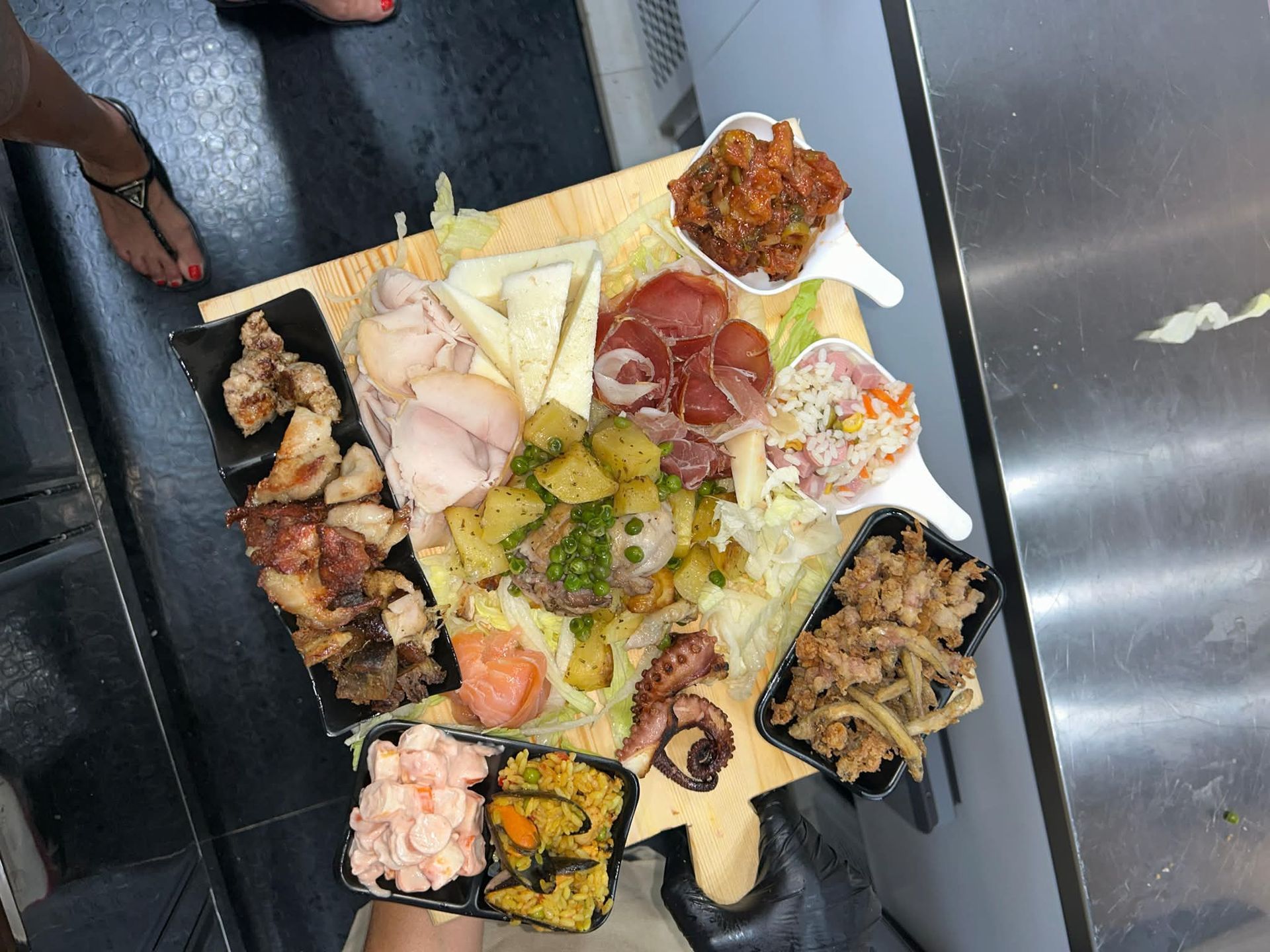 Un assortimento di antipasti e tapas su un tagliere nero, con salse, salumi, frutti di mare e stuzzichini fritti.
