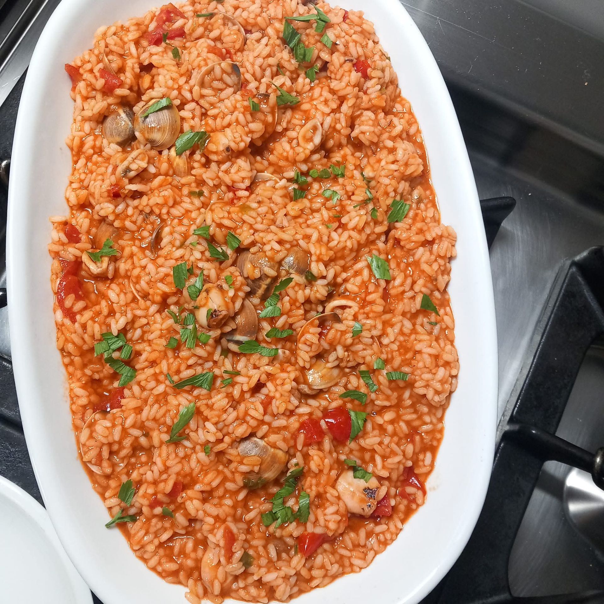Piatto ovale di riso rosso con verdure ed erbe aromatiche sul fornello