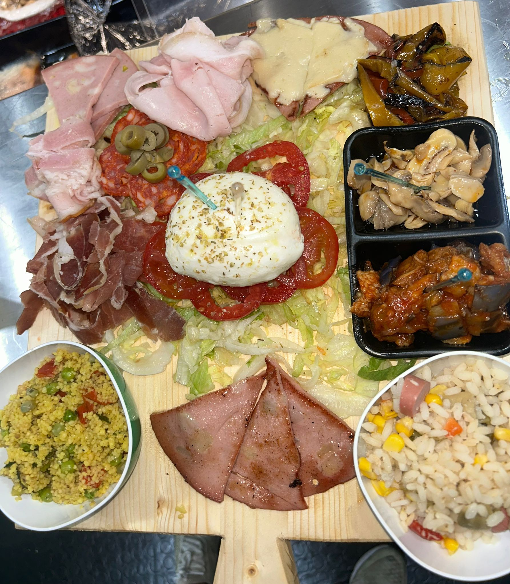 Tagliere di salumi e formaggi assortiti, olive, insalata di pasta e contorni di verdure su un tagliere di legno.