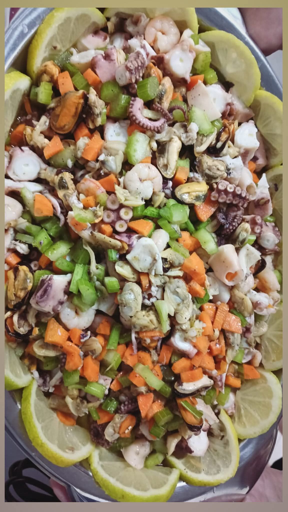 Insalata di frutti di mare con verdure a dadini, servita su un piatto foderato con fette di limone.
