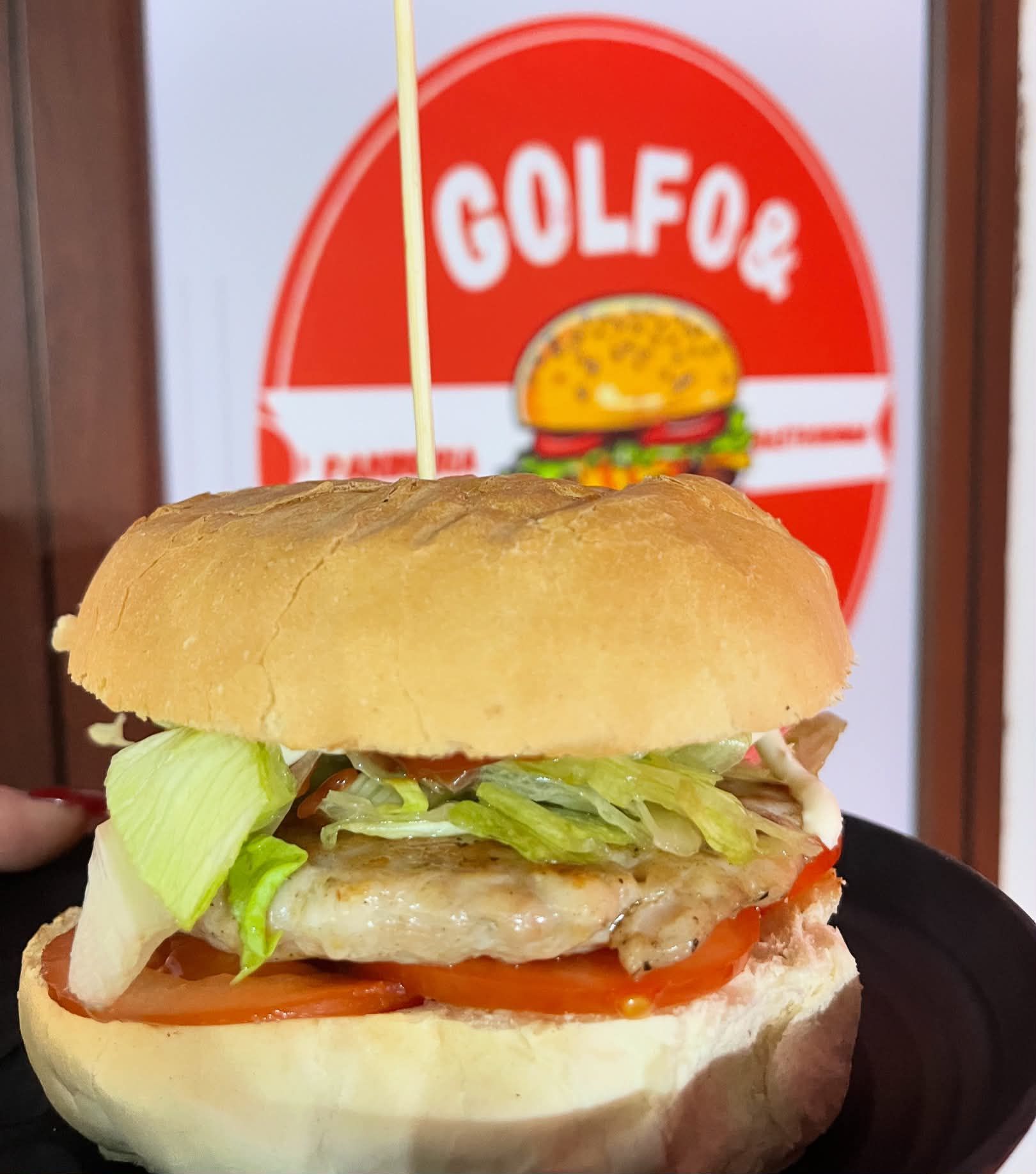 Primo piano di un hamburger con lattuga su un piatto nero davanti a un'insegna GOLFOE.