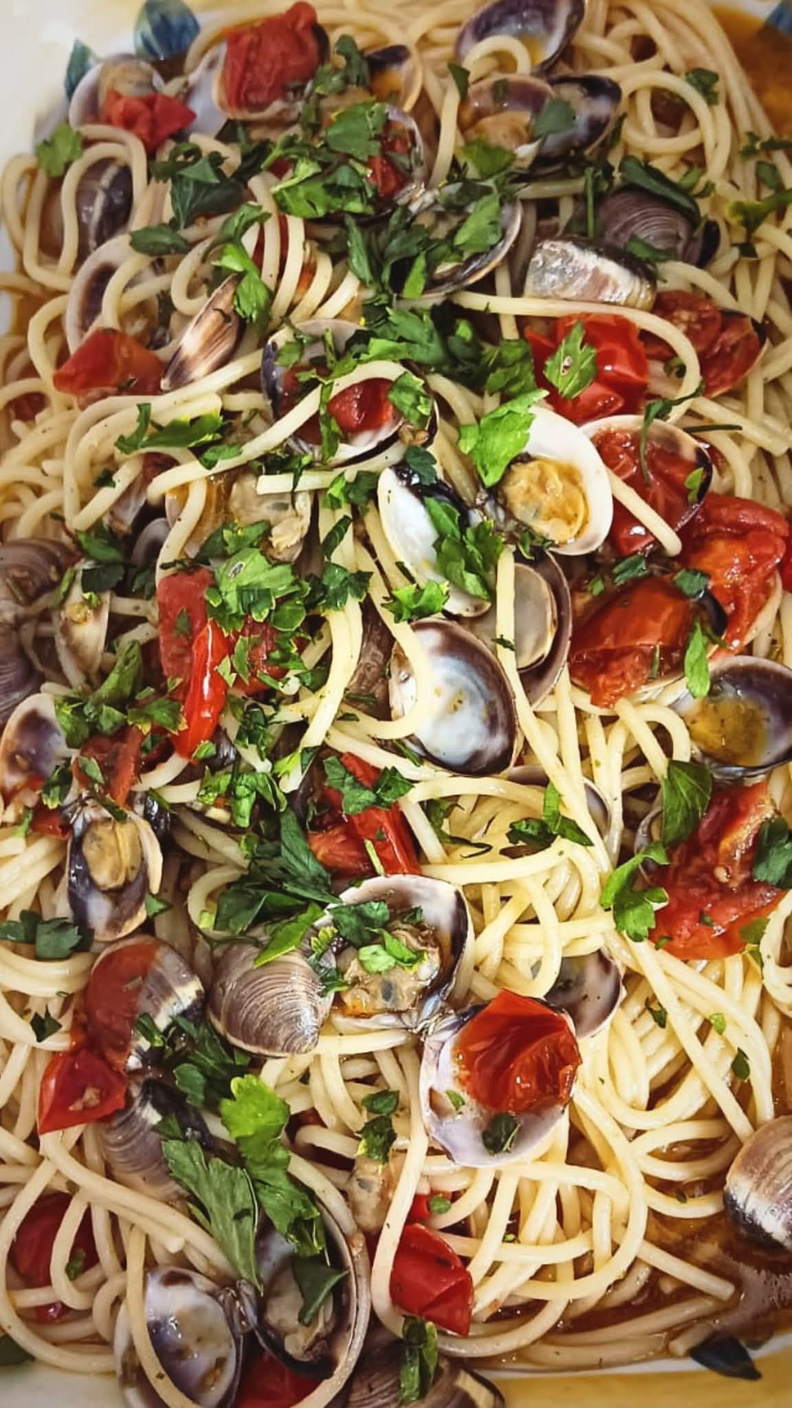 Spaghetti con vongole, pomodorini ed erbe aromatiche in un piatto da portata bianco.