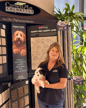 A woman is holding a puppy in front of a display of carpets.