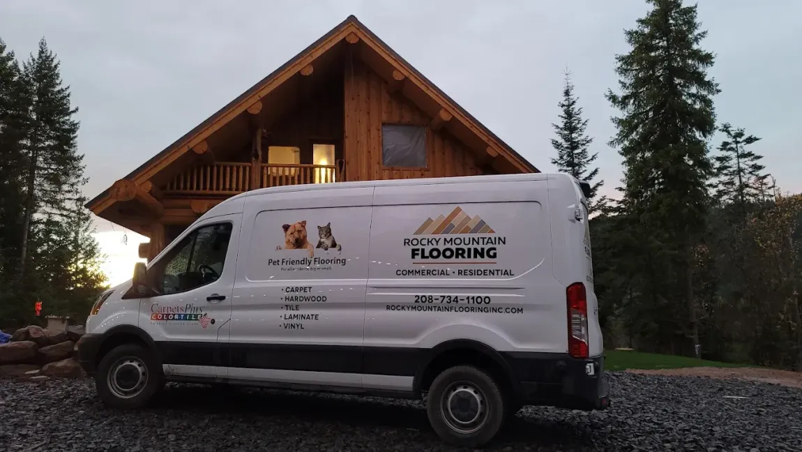 A white van is parked in front of a wooden house.