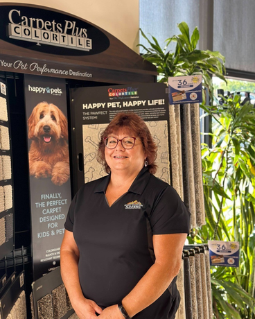 A woman is standing in front of a carpets plus color tile display.