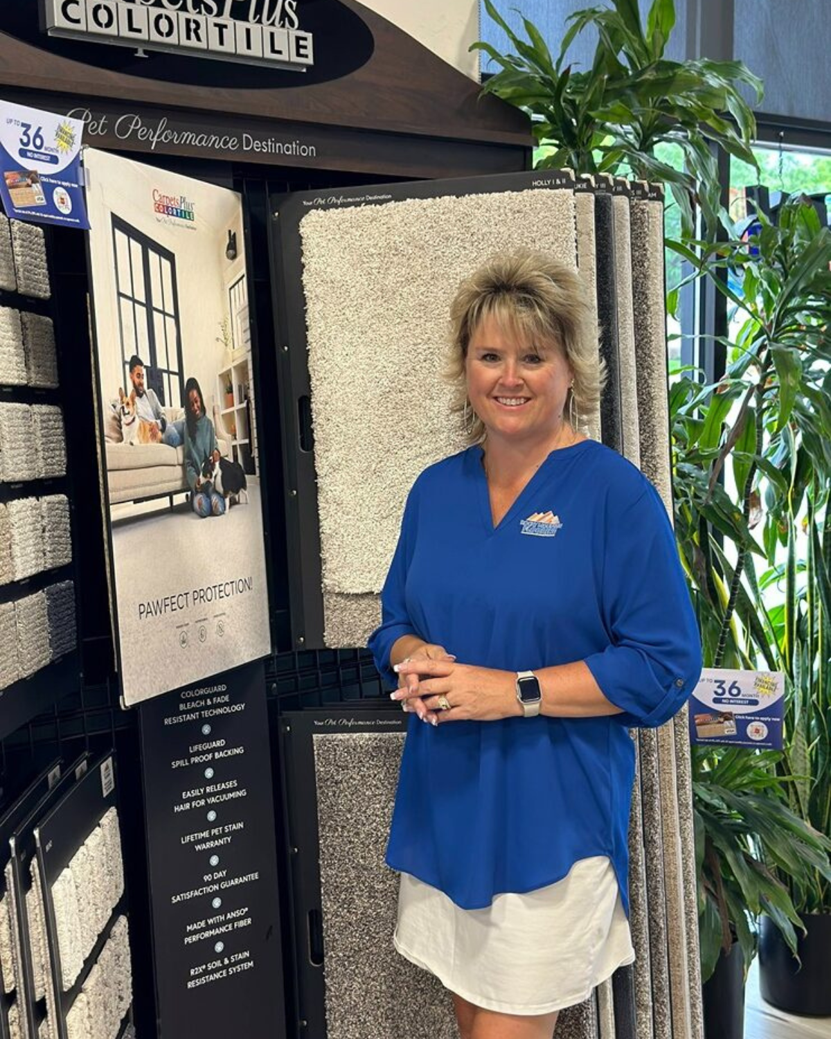 A woman in a blue shirt is standing in front of a display of carpets.