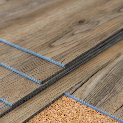 Stack of wood-look flooring planks, light brown with visible wood grain, on a cork underlayment.
